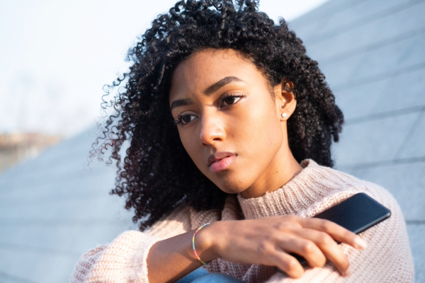 Black woman sitting on roof holding phone after experiencing the comparison trap.