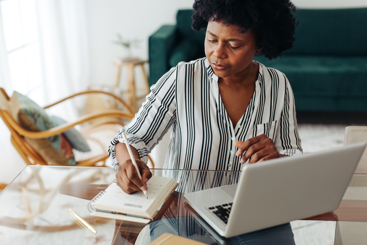 Black woman at table writing out goals in notebook.