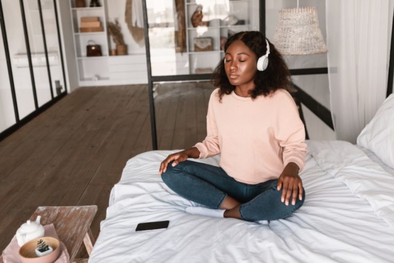 Black woman practicing mindfulness while meditating on top of bed.