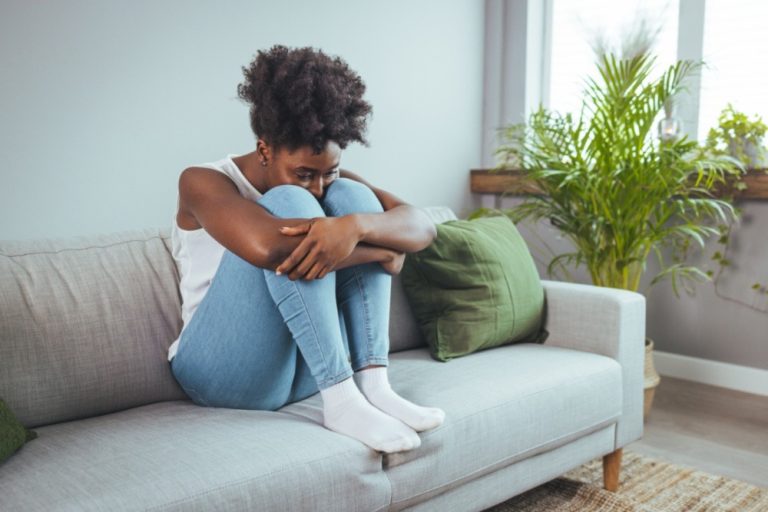 black woman with knees pulled to chest while considering major life changes