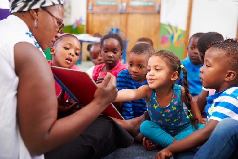 Black teacher shows book to students.