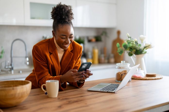 Black woman happily engaging with her audience on her phone at kitchen island.