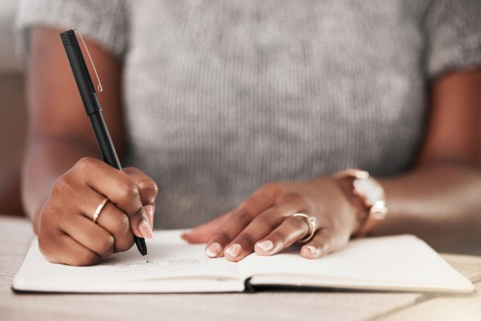 Black woman's hands writing goals in journal