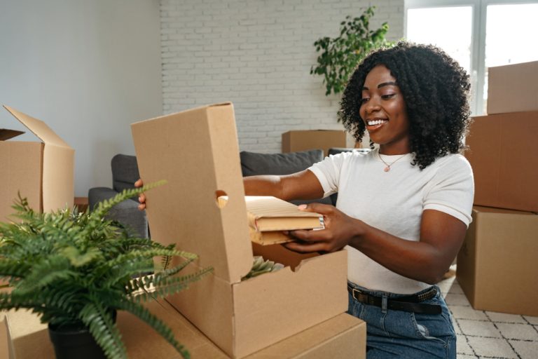 Young Black woman tapped into her creativity after relocating seen taking book out of box.