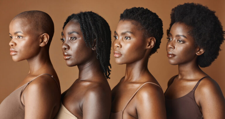 Four Black women of various skin colors standing facing one way.