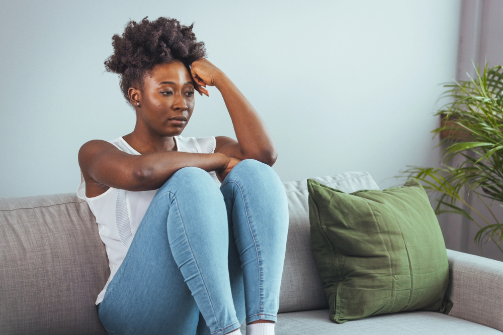 Black woman on sofa looking as if she is battling with her mental health.