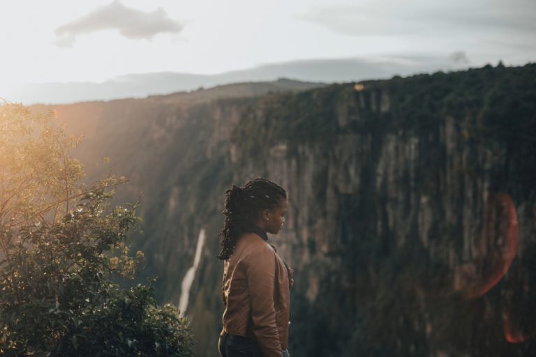Black woman on mountain ledge symbolizing consistency.