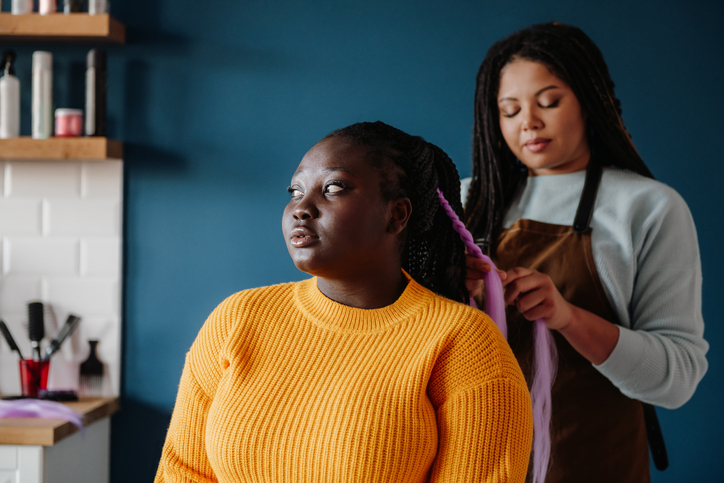 Black woman braiding another Black woman's hair in a protective style