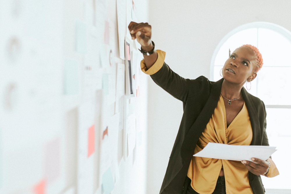 Black woman doing a brain dump on a white board based on her business pillars.