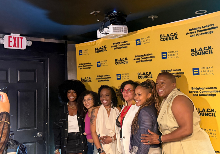 Group of diverse attendees smiling for a photo in front of a yellow B.L.A.C.K. Council backdrop.