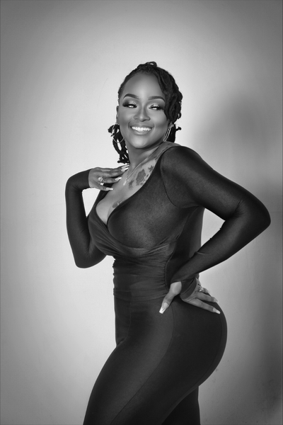 Smiling woman in a fitted black dress posing with one hand on her hip in a black-and-white photo.