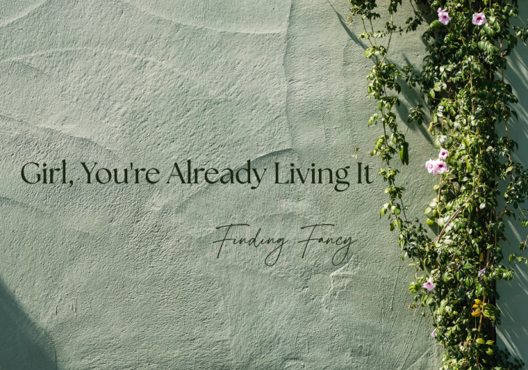 Decorative green wall with pink climbing roses on the right and the text: 'Girl, You're Already Living It' with 'Finding Fancy' in cursive.
